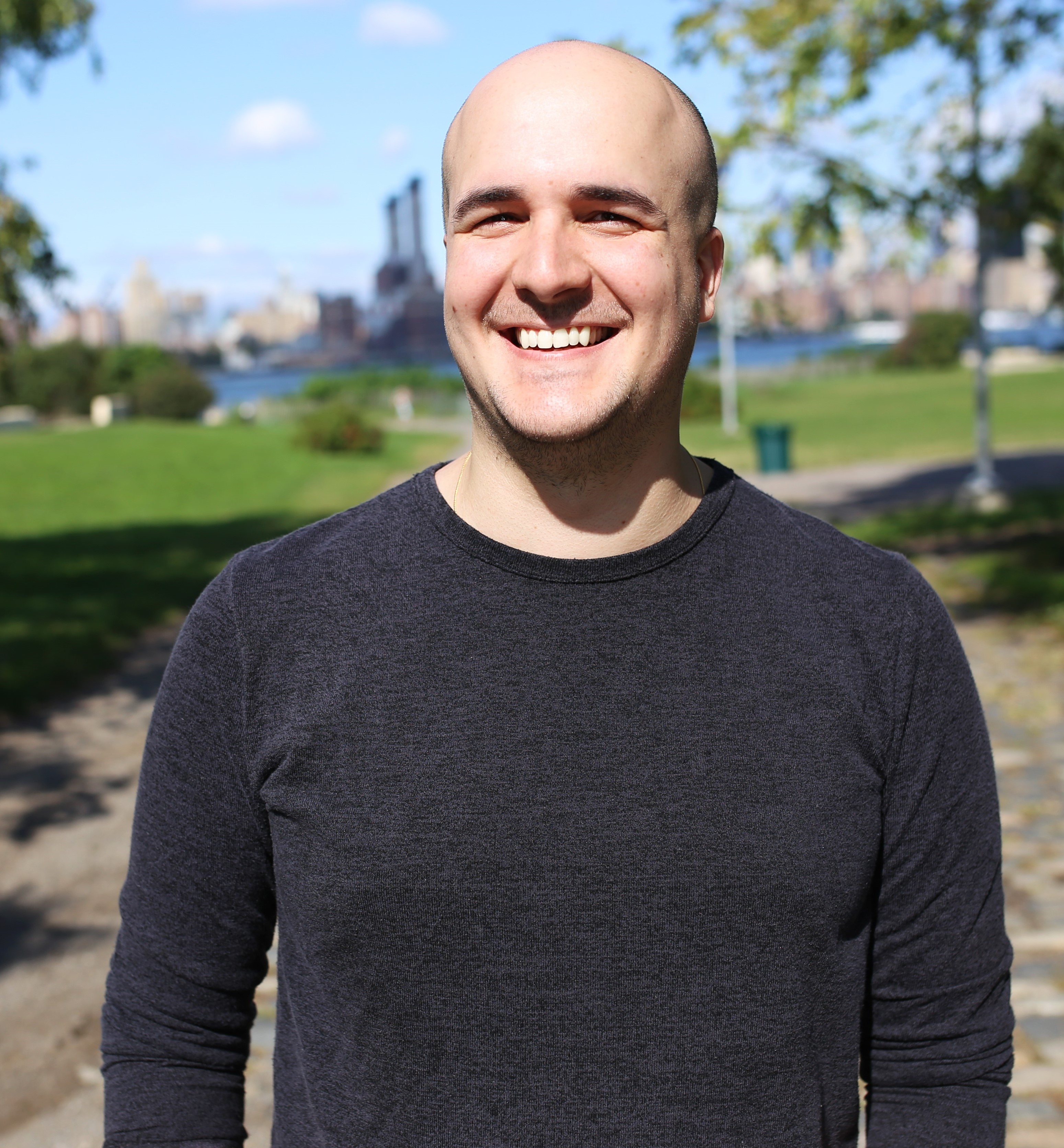 Smiling man with city buildings and path in the background.